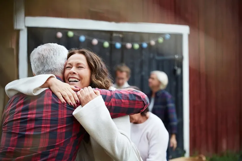 A daughter hugging her father at a family gathering outside his home
